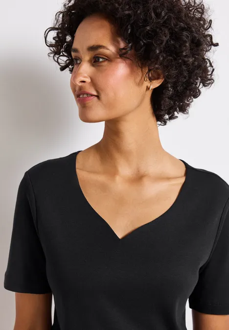 Frau mit lockigem Haar und schwarzem V-Ausschnitt-Shirt schaut zur Seite.